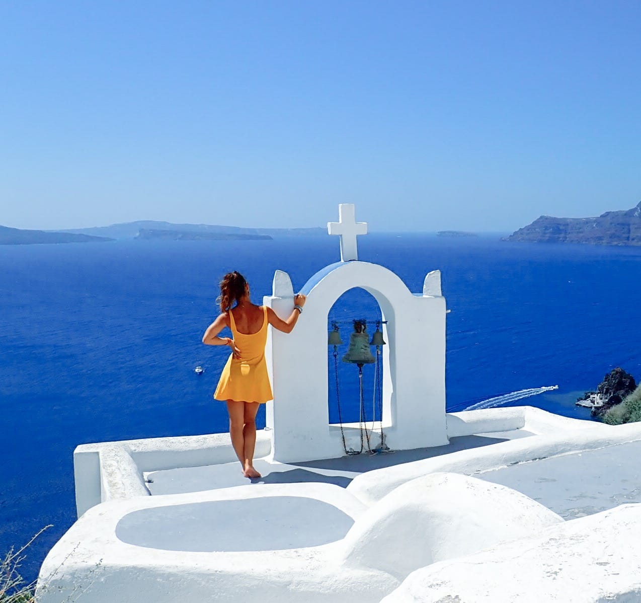 woman in yellow dress standing on the roof of a church looking out at the oceani in Santorini Greece