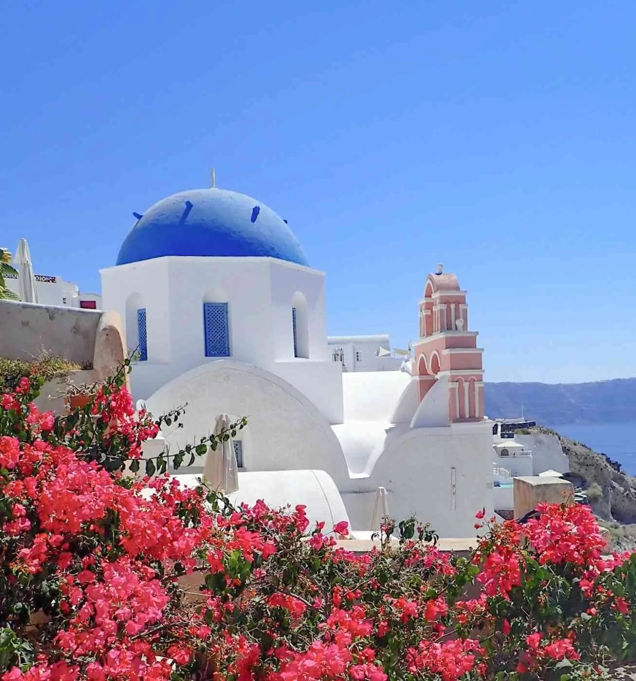 a blue domed and white washed chapel with a pink bouganvillea in santorini greece