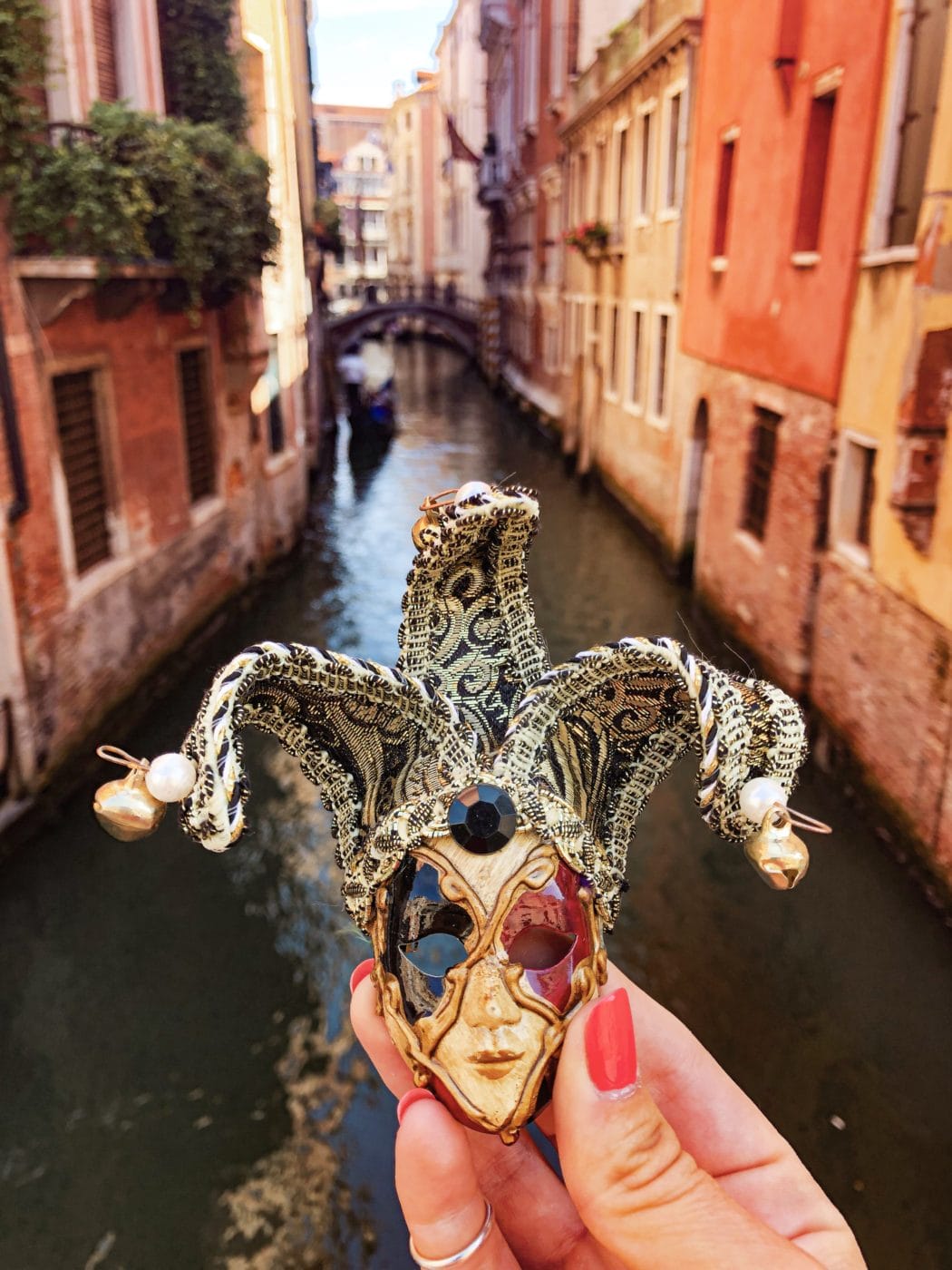 a woman hand holding a souvenir miniature authentic venetian mask with the canal in the background in venice italy
