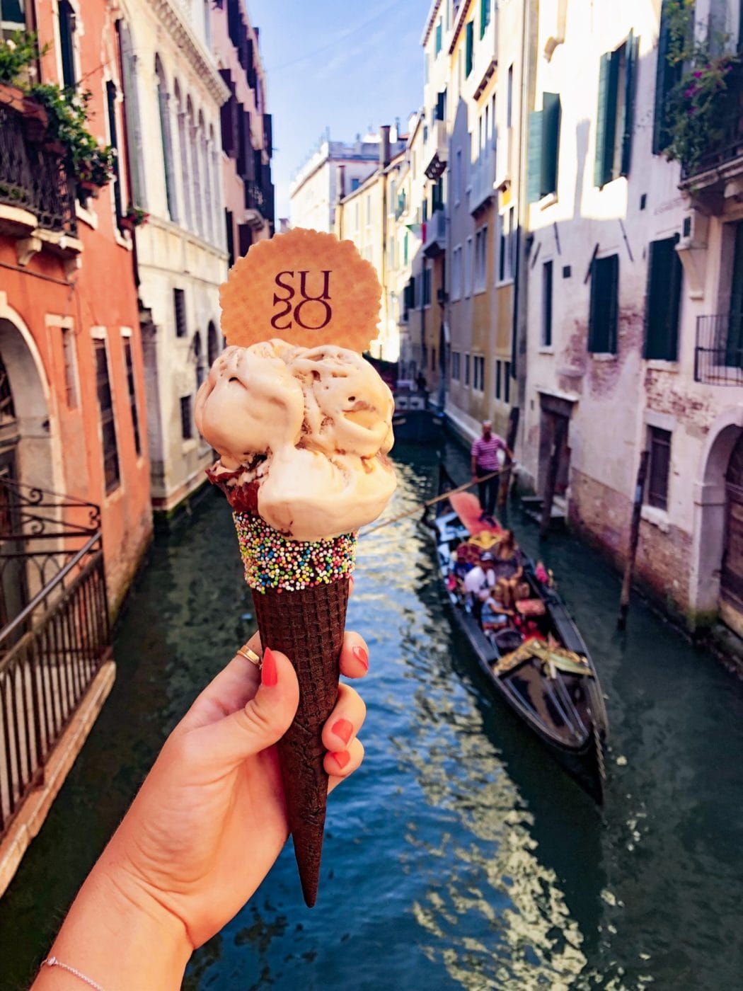 Woman hold holding a scrumptious gelato with sprinkles with a gondola in the background in venice italy