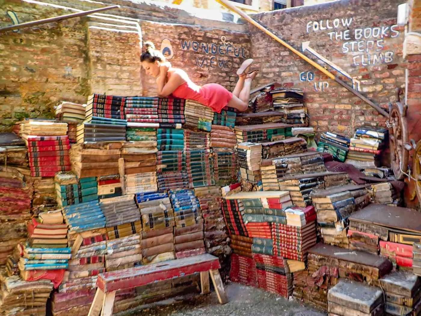 woman reading perched on top of a staircase made of books at the Acqua Alta bookstore in Venice, Italy