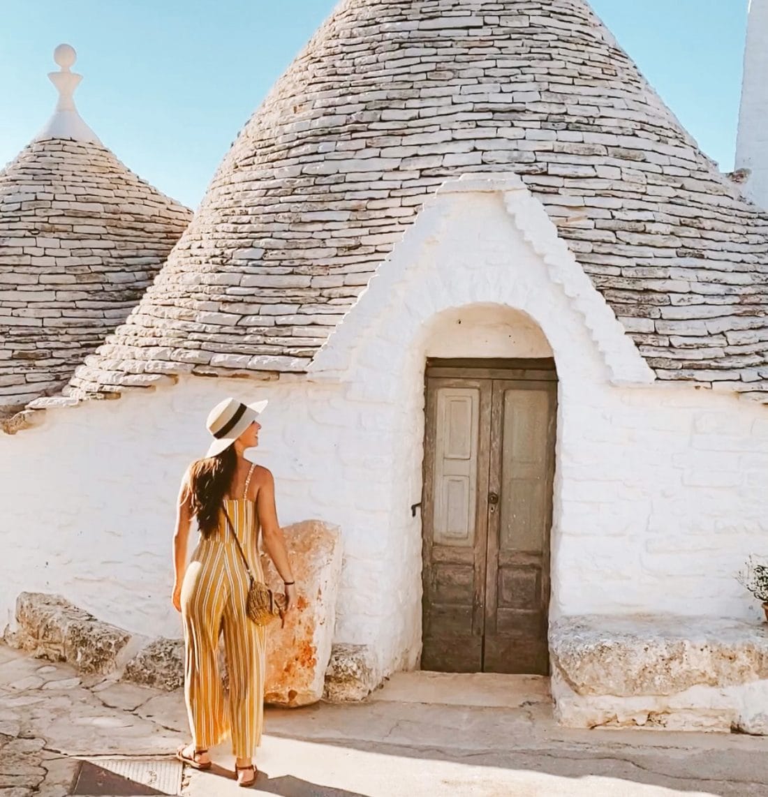 A woman in yellow dress and hats wandering around the alleys of Alberobello exploring the trulli