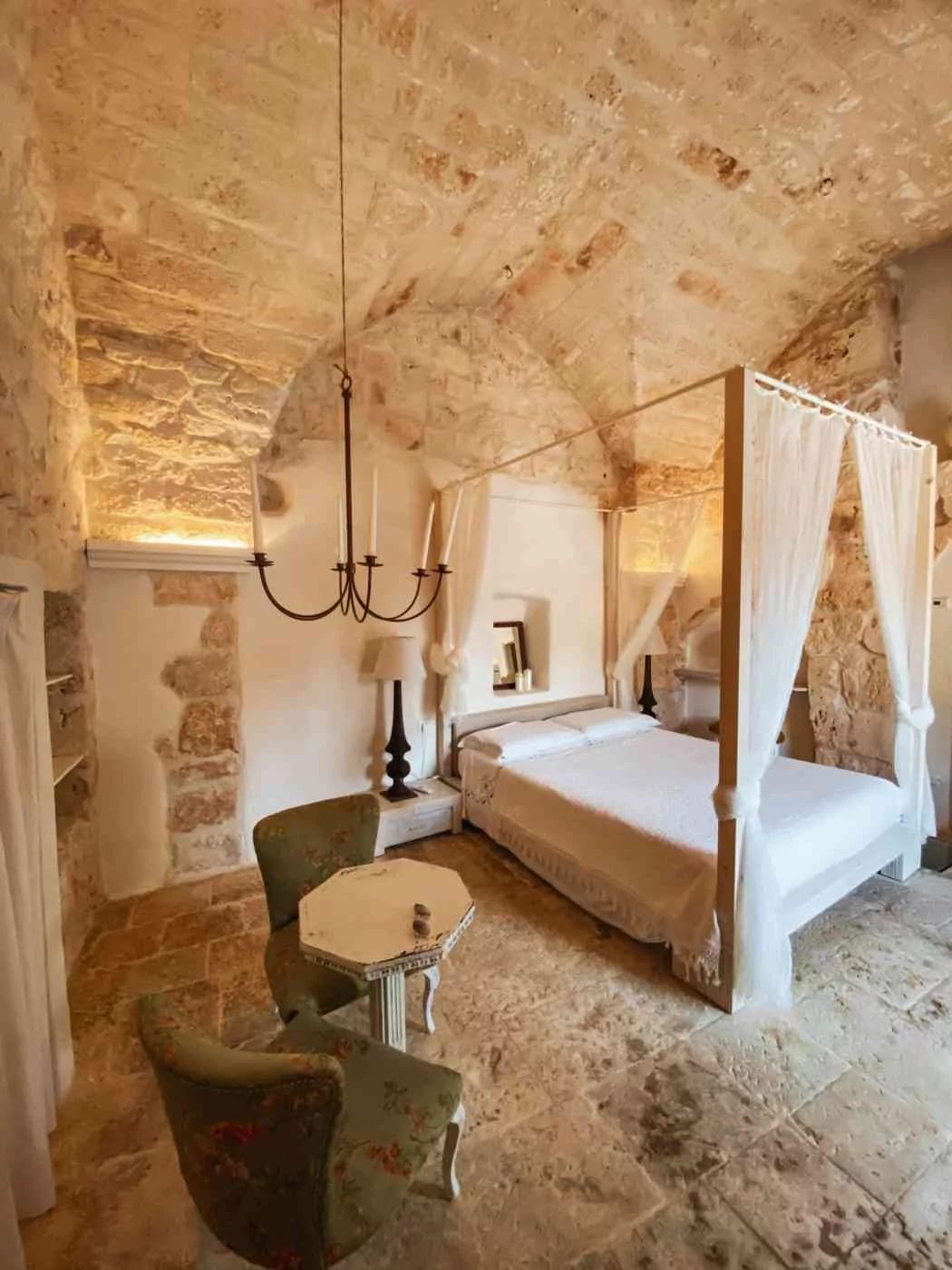 stone-finished room with large king bed and hanging chandelier- room of relais grottone B&B in Ostuni, Puglia