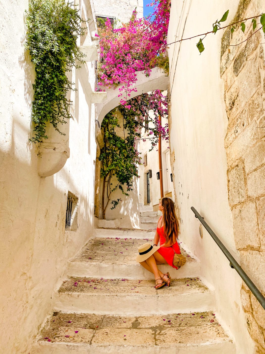 a woman in a red dress sitting down on a limestone staircase in the alleys of Ostuni puglia