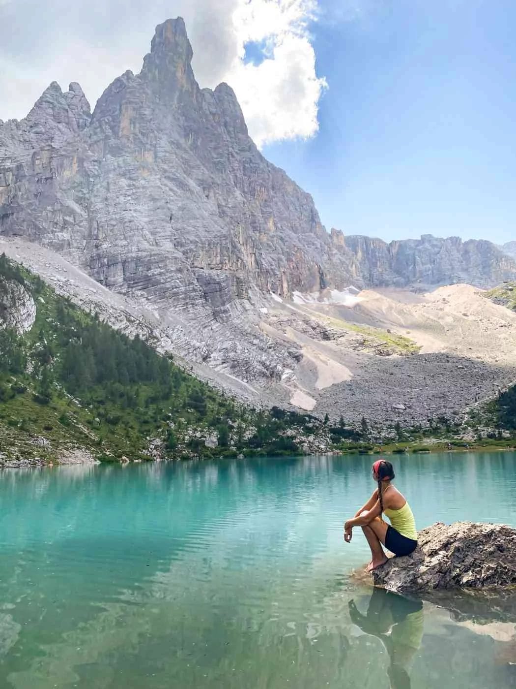 woman kneeling on a rock on the banks of turquoise and milky colored lake sorapis in the italian dolomites