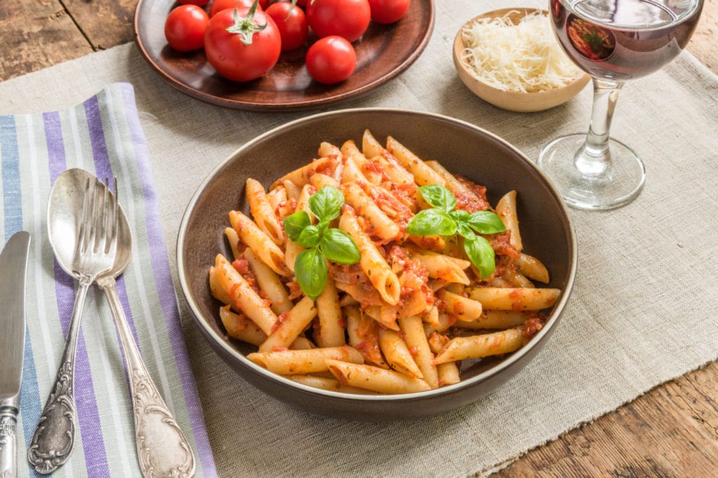 Pasta All'Arrabbiata, penne with tomato sauce, basil, parmesan cheese plated and served in a brown bowl
