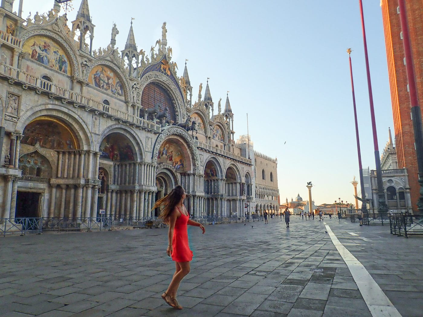 woman in red dress wandering around saint mark's square in venice right in front of the basilica.