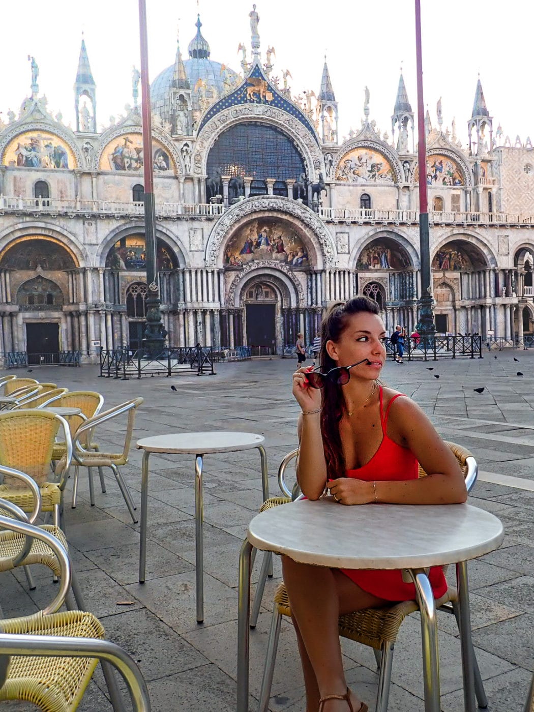 a lady sitting at a cafe table in saint mark's square right in front of the basilica in venice, italy