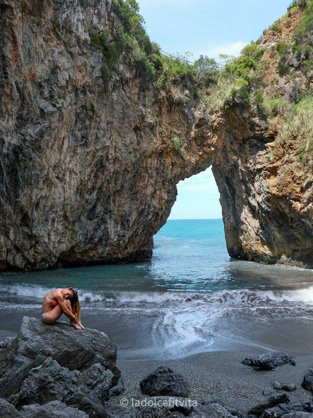 A girl on a rock posing at the beautiful Arcomagno Beach in Calabria, Italy