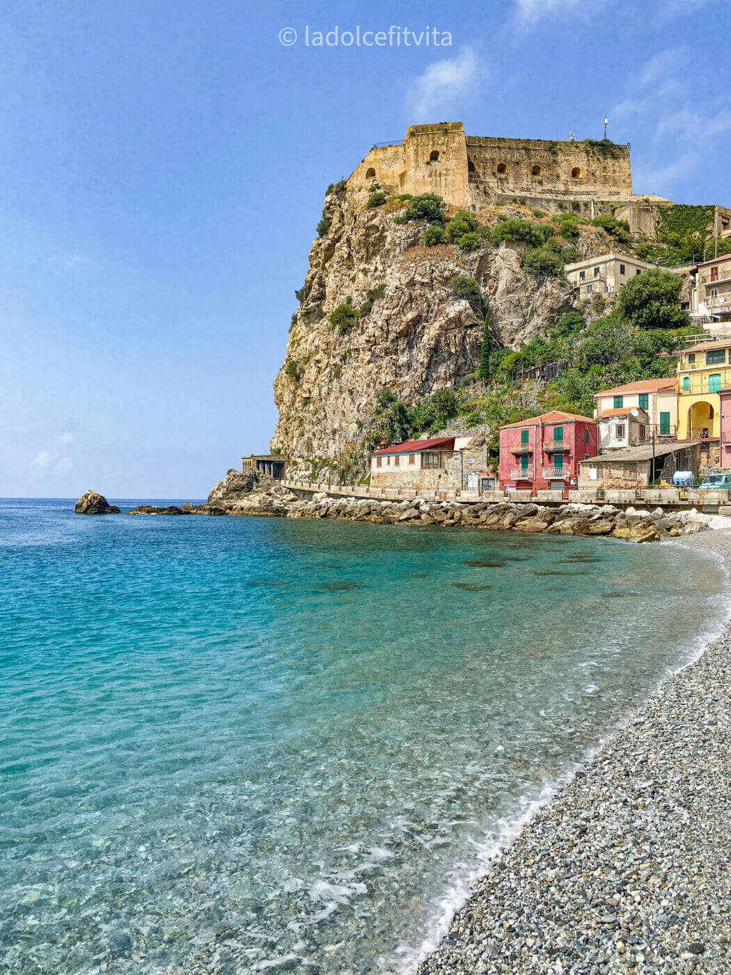 Castello Ruffo on a cliff overlooking turquoise sea waters and pebbly beach in Scilla - Calabria, Italy