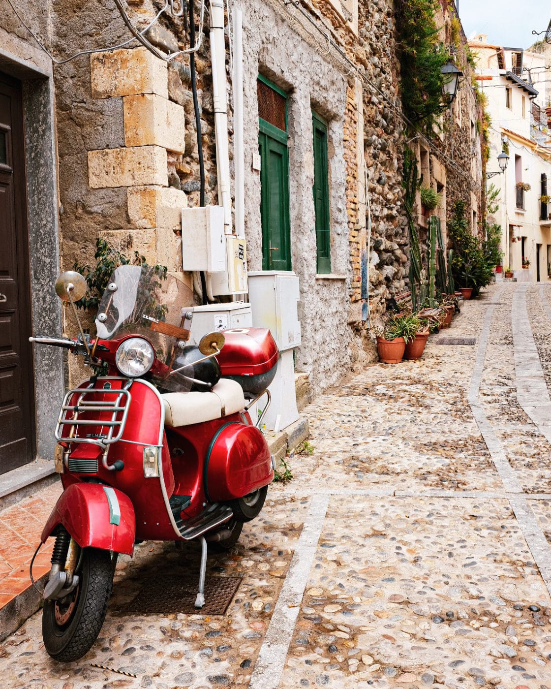 a red vespa parked in a cobblestoned street in Calabria