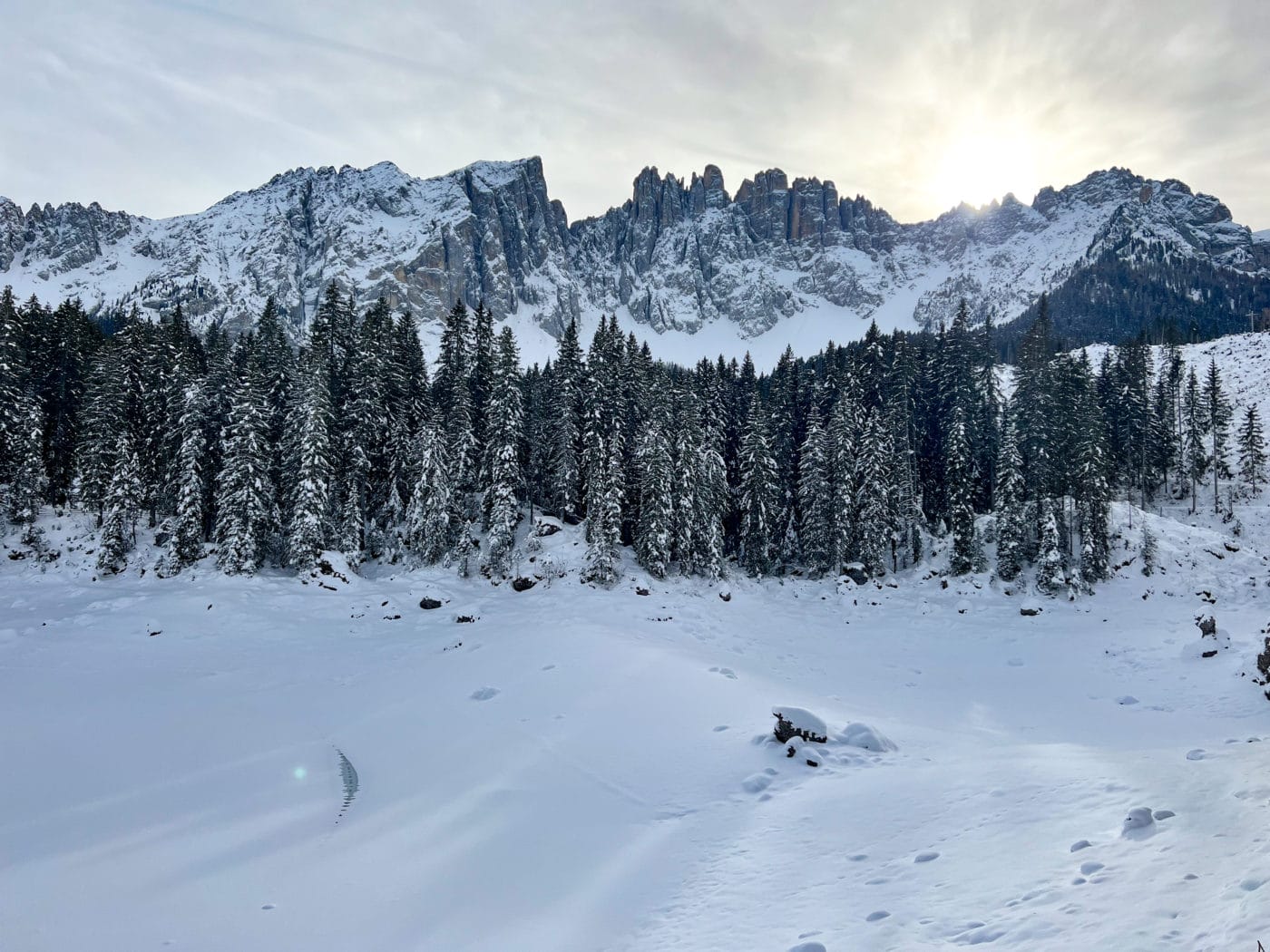 Lago di Carezza in Dolomites Italy frozen in the winter with snowy pine trees and snowcapped mountains in the background