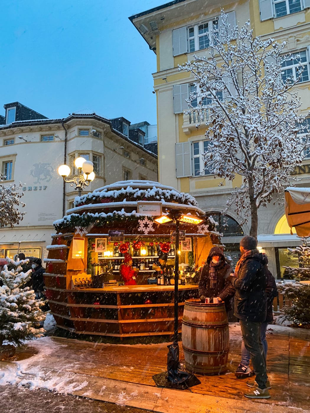 two men sipping at mulled wine at a stall at the bolzano christmas market in Italy under the snow