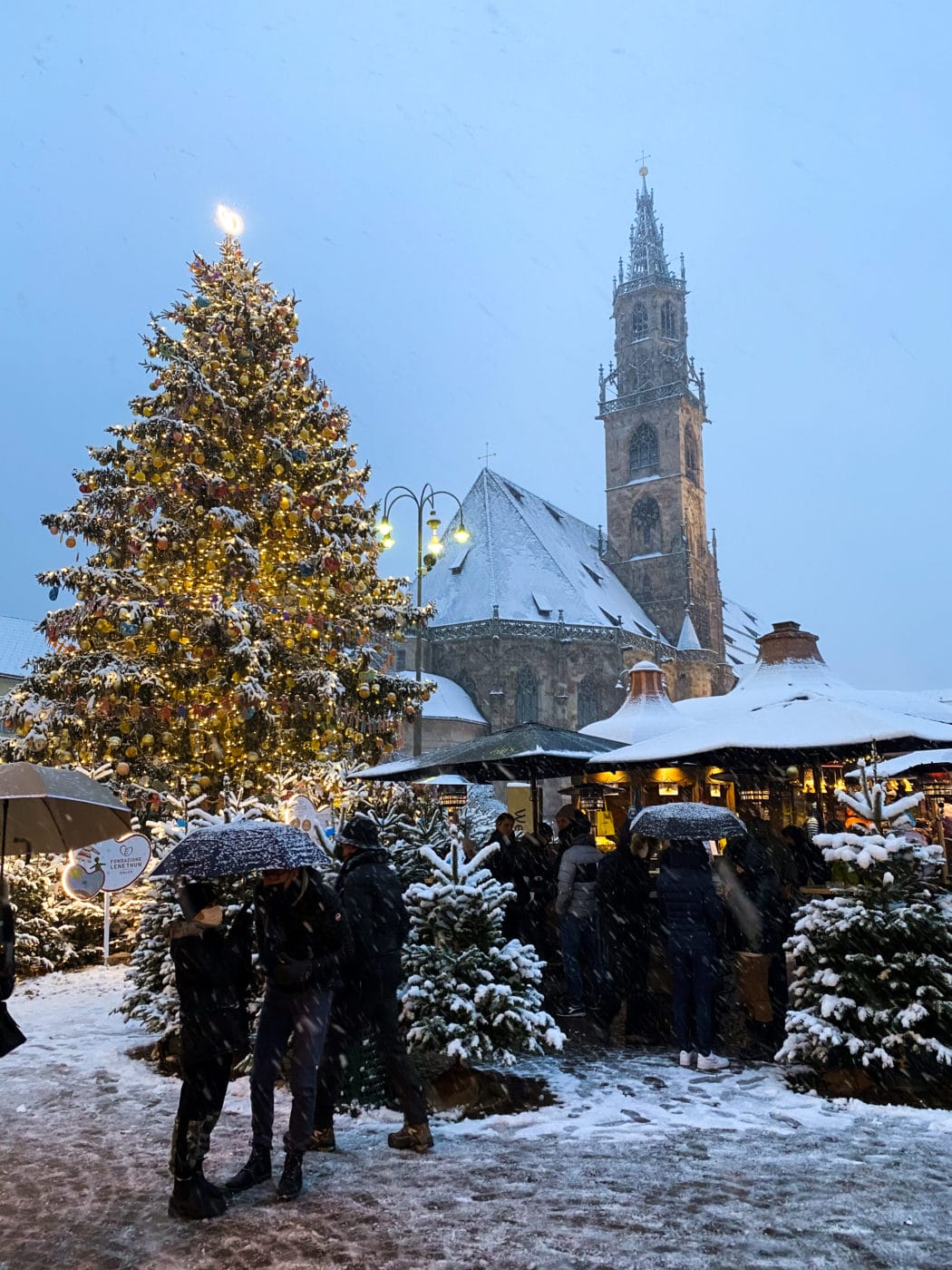people huddling under the snow in bolzano at the main square with a big chirstmas tree in the background