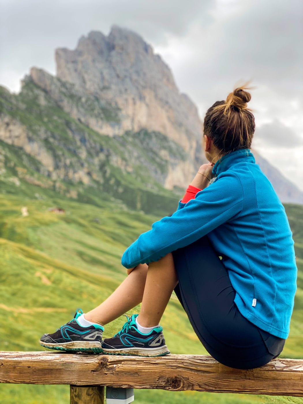 closeup of a hiker in blue sweater sitting on a fence looking at the dolomite mountains