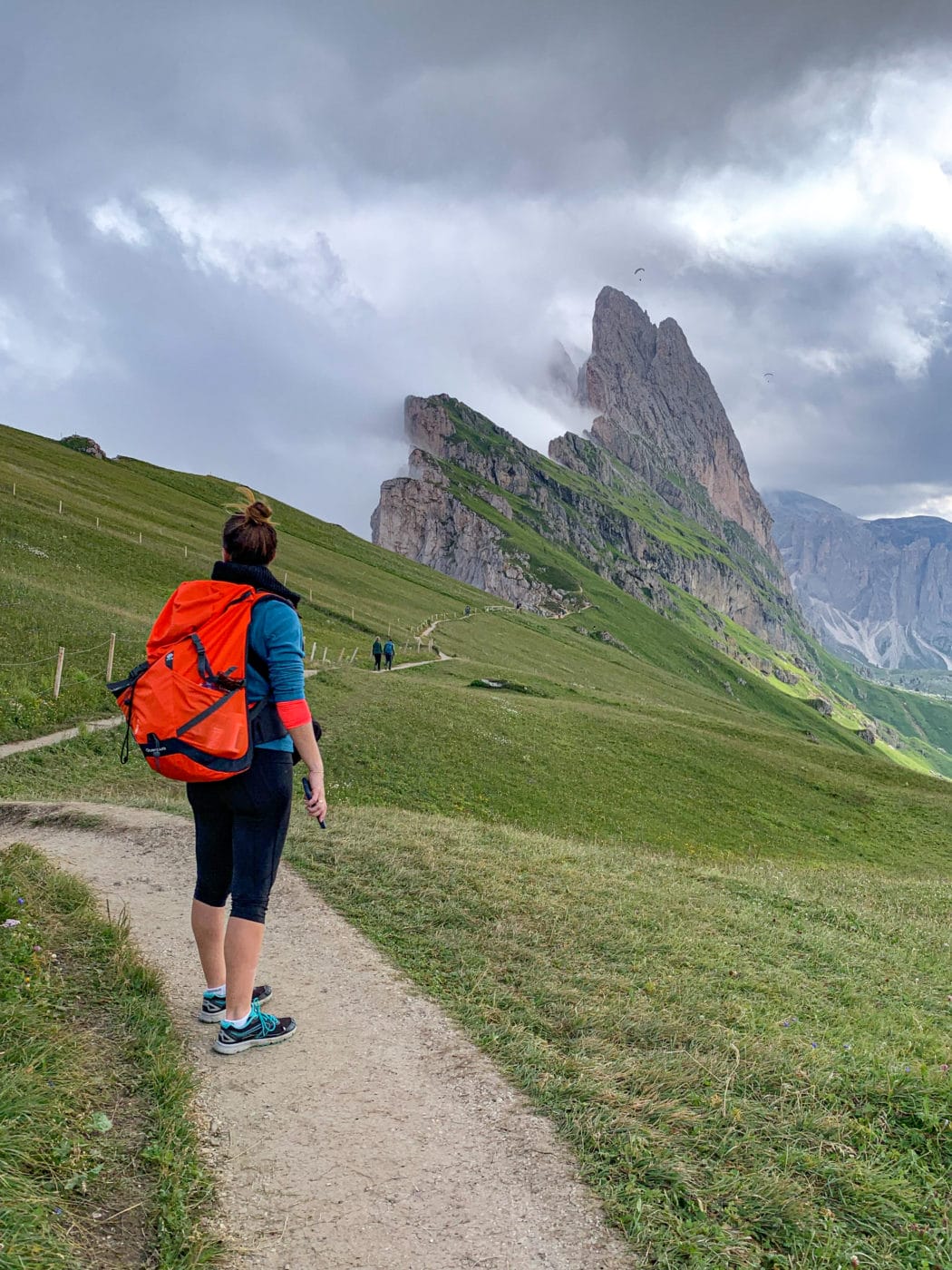 hiker with a backpack on a trail looking at the Seceda mountain in the background