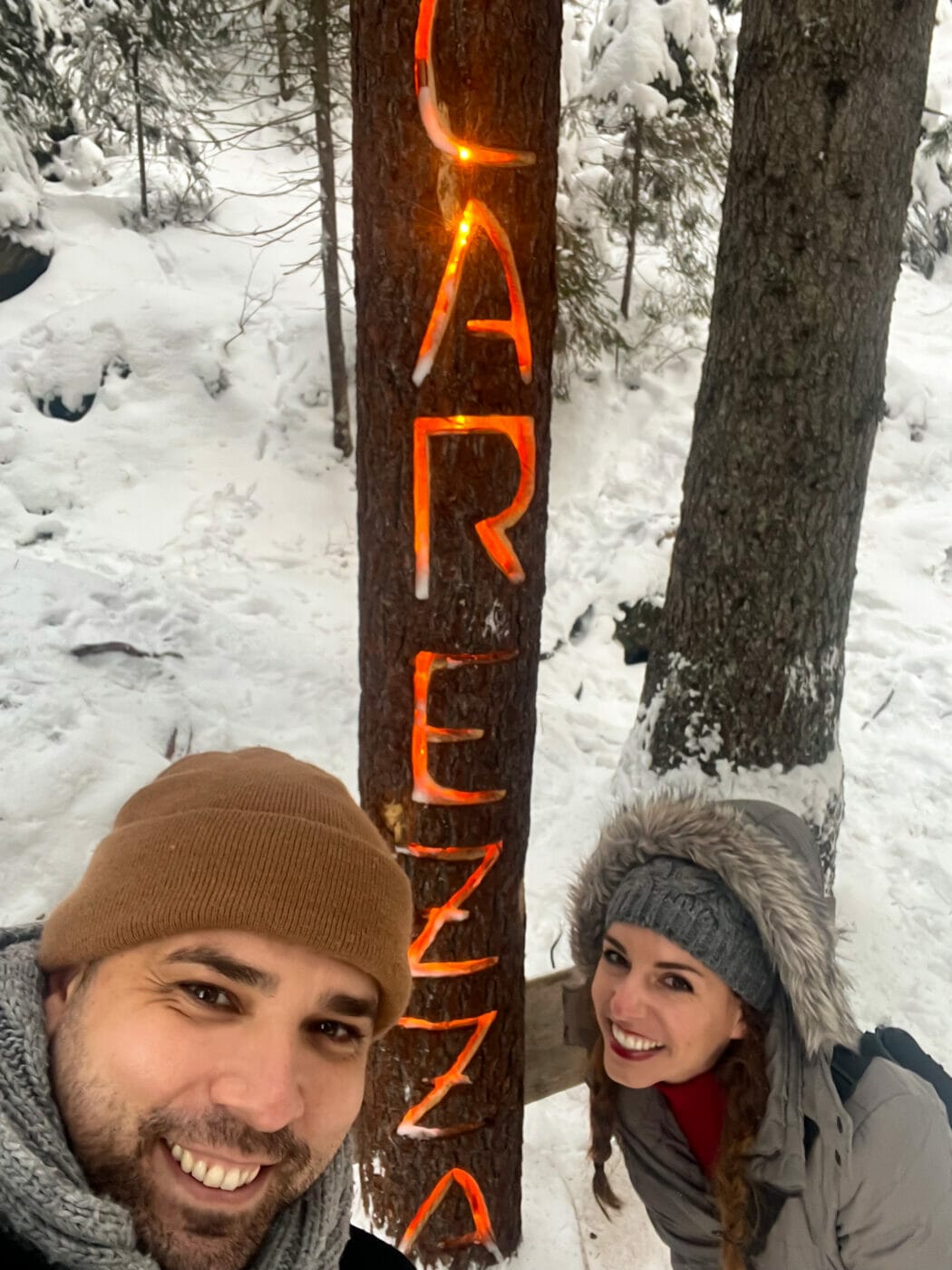 a couple posing for a selfie in front of the Carezza lake wooden sign in the Dolomites Italy.