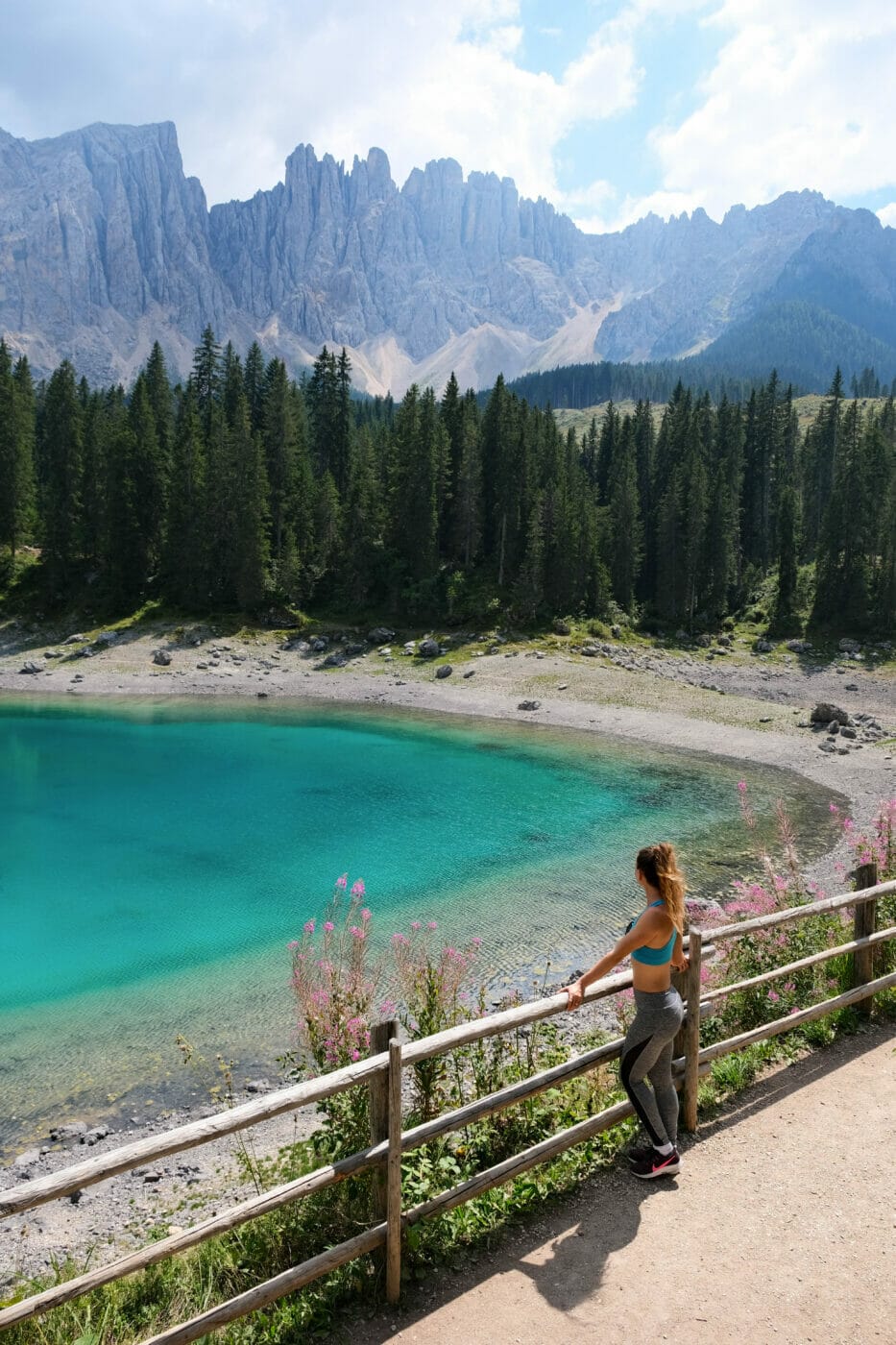 woman standing on the trail of the lago di carezza hike in the dolomites as she gazes onto the beautiful emerald lake