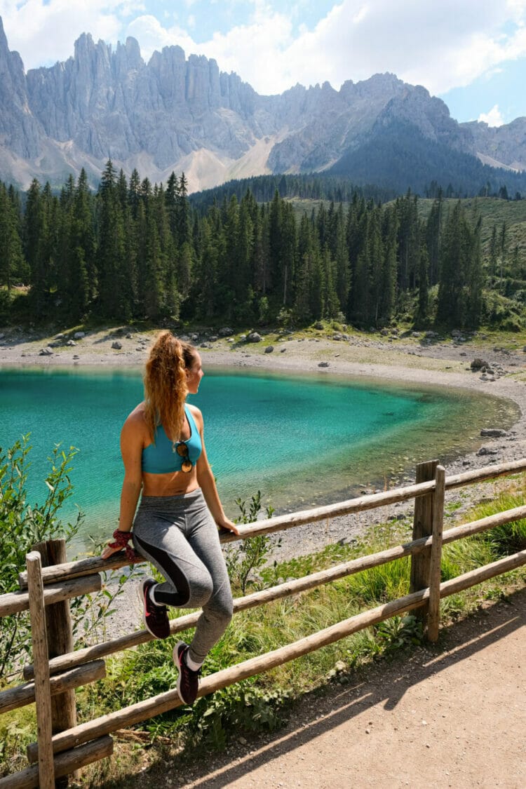 woman sitting on the fence around the beautiful turquoise Lago di Carezza in the dolomites Italy