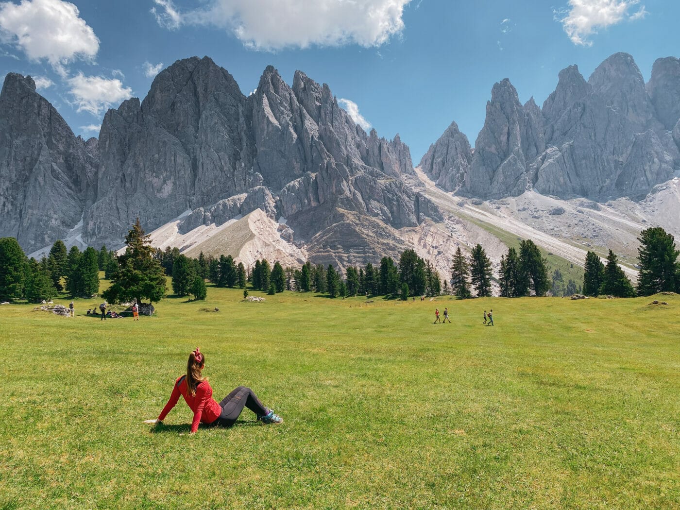 a woman sitting in a meadow gazing at the Odle peaks of the Dolomites in Italy