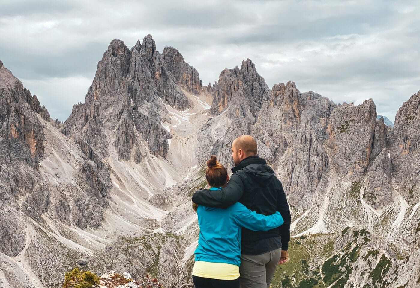 a couple standing on the edge of a cliff embracing romantically and gazing at the mountain peaks of the Dolomites, Italy