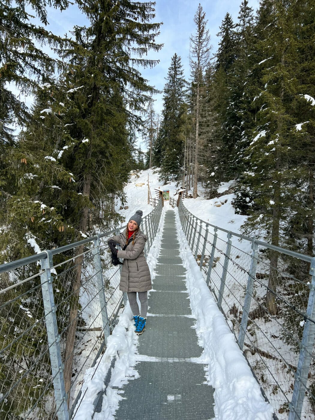 girl posing for a photo on a snowy suspended bridge while on the Lago di Carezza hike in Italy