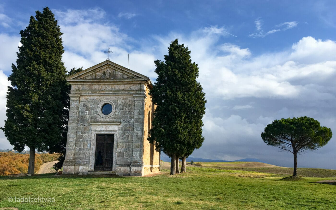 the tiny and charming chapel of Vitaleta framed by two cypress trees in the hills of the tuscan countryside