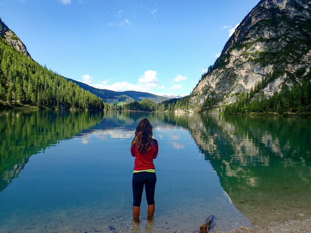 woman from behind standing in red shirt gazing out on Lake Braies in the Italian Dolomites
