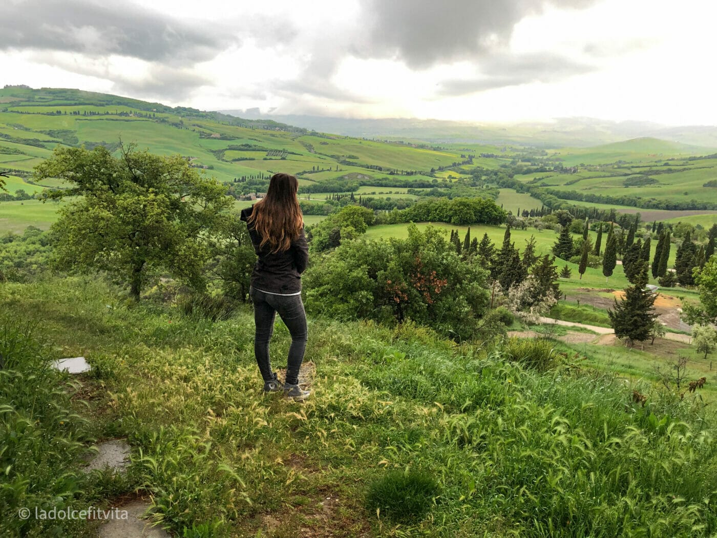 woman gazing out on the lush green couyntryside below from atop a hill in Tuscany