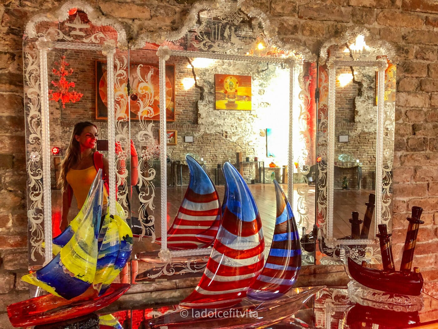 a woman taking a selfie in a mirror with glassware pieces on display in Murano, Italy