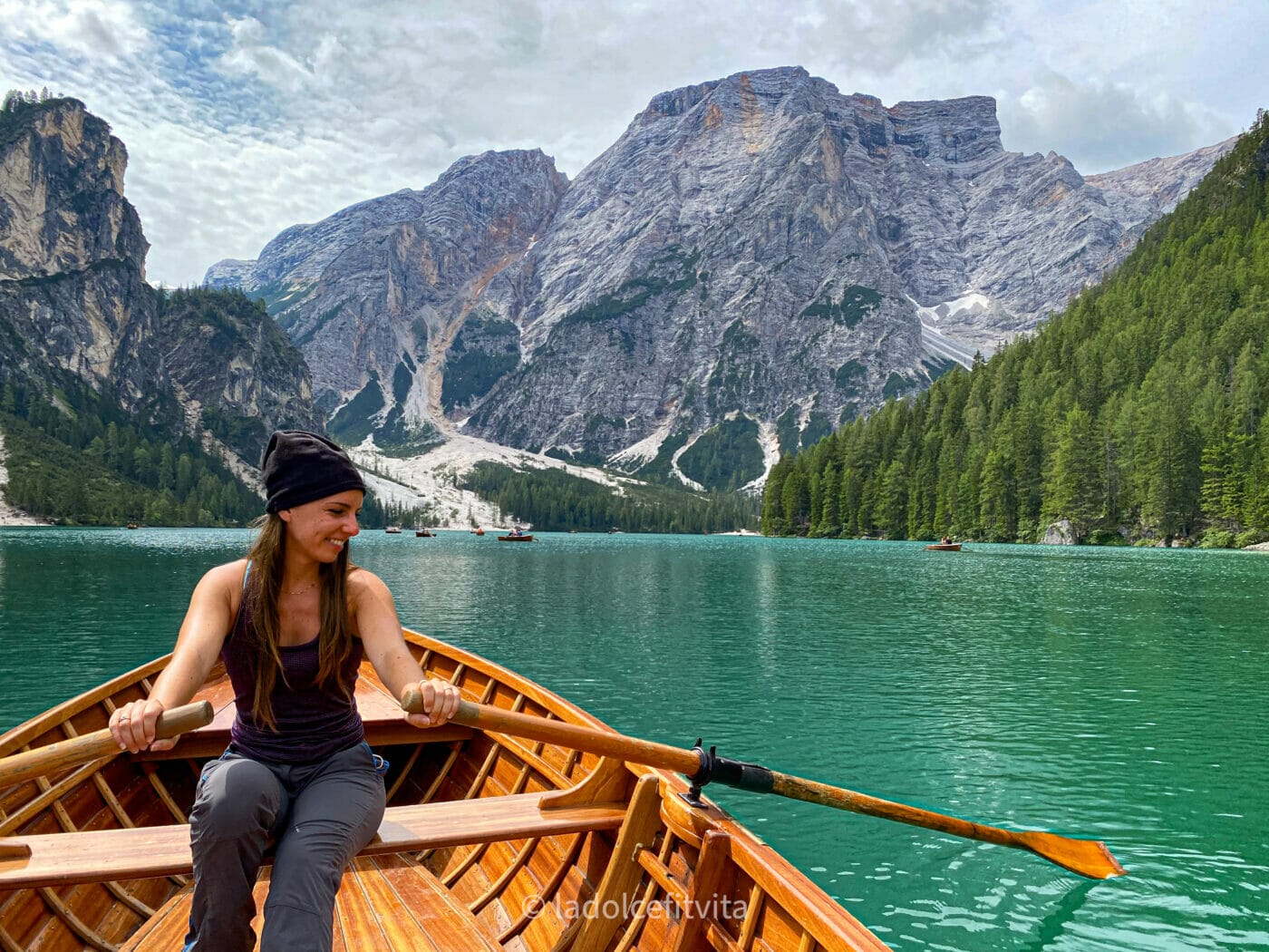 woman rowing a boat in lago di braies, the emerald lake of the dolomites