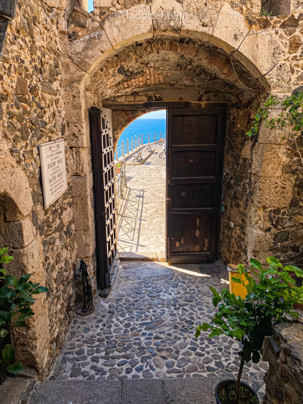 the view of a vibrant turquoise sea as seen through an open door in a courtyard in southern Italy