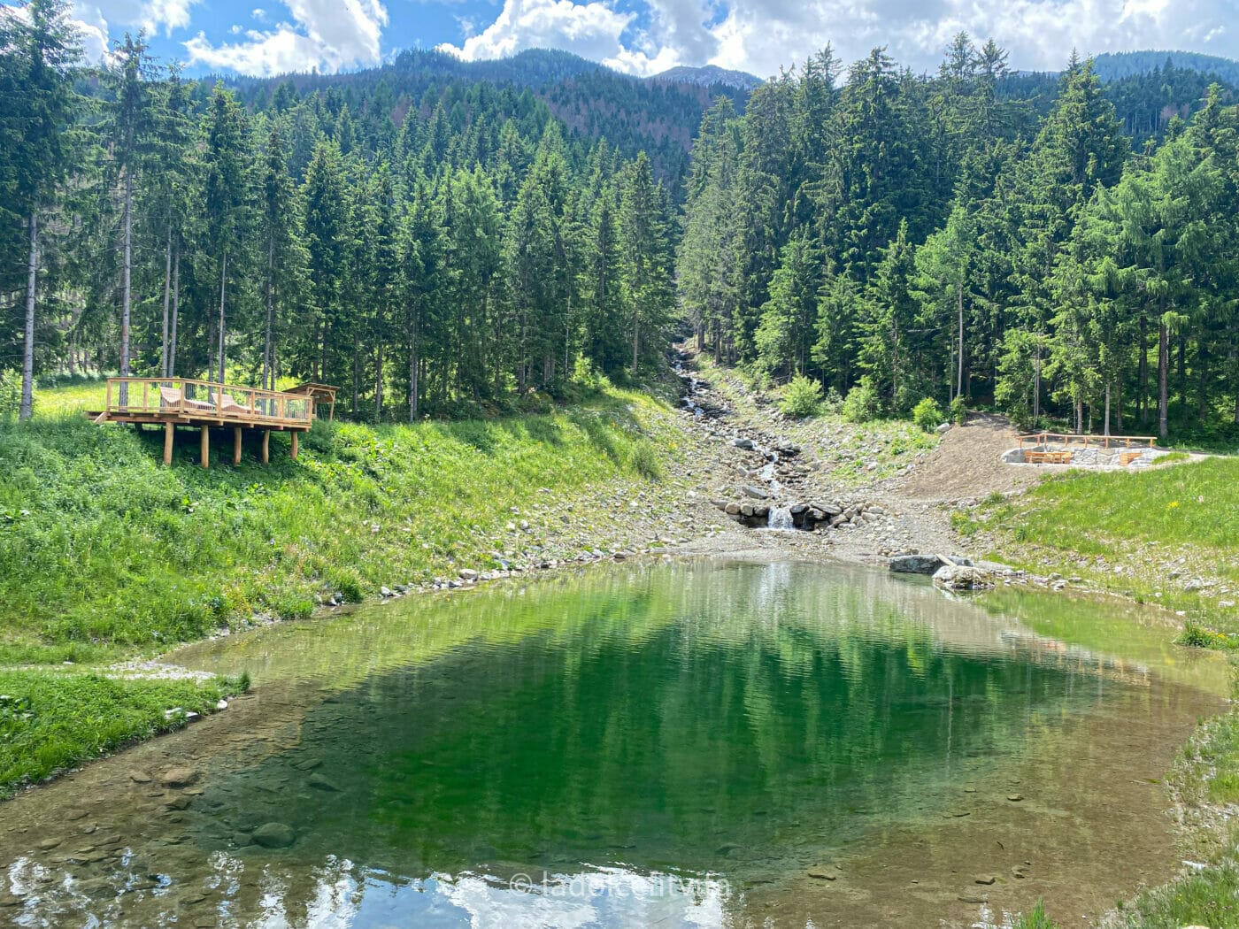emerald pond and wooden view deck along the Dobbiaco Lienz cycling Route that crosses the Italian-Austrian border