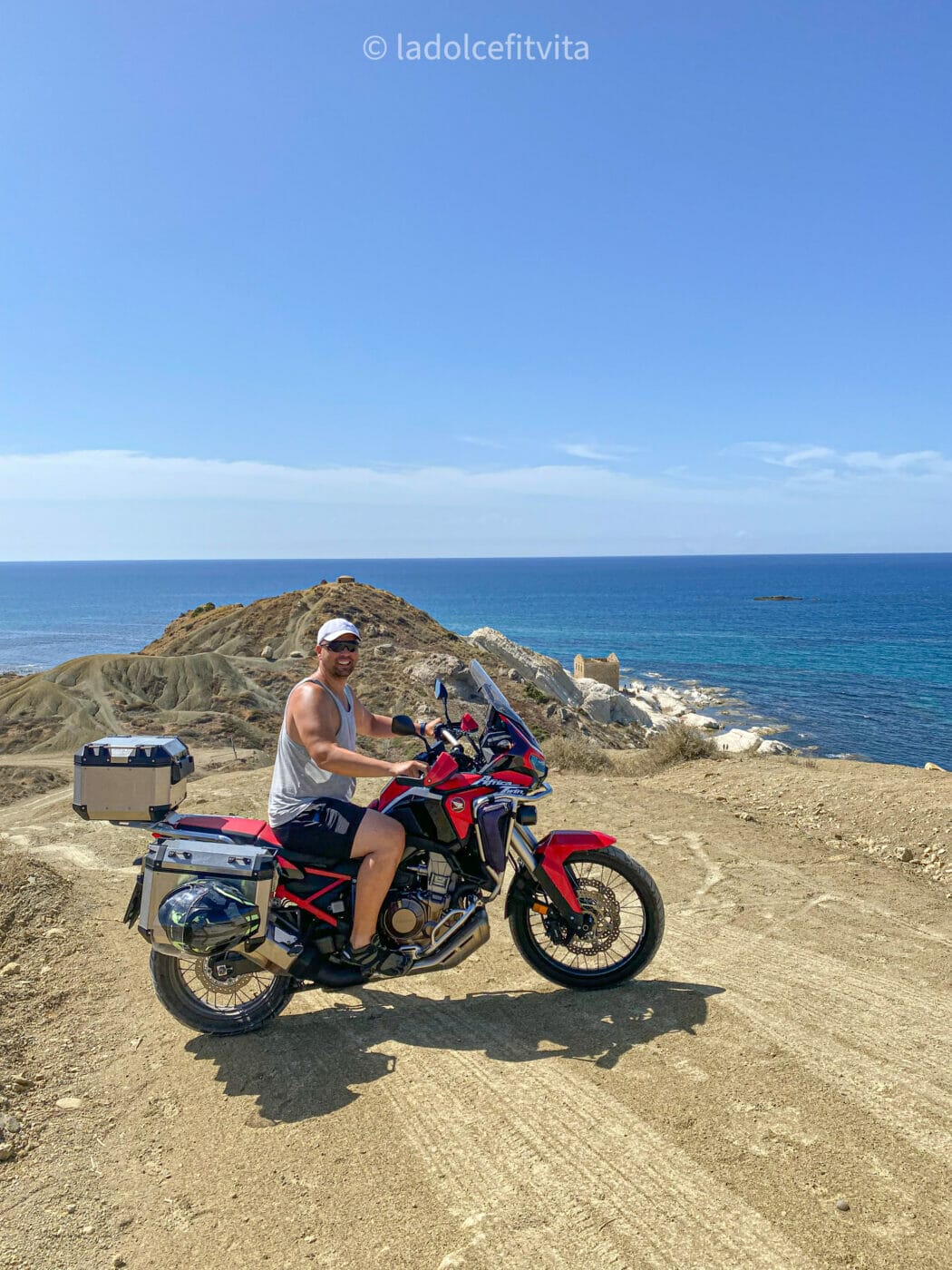 man on motorcycle on a dirt road on a cliffside towering over the Mediterranean sea