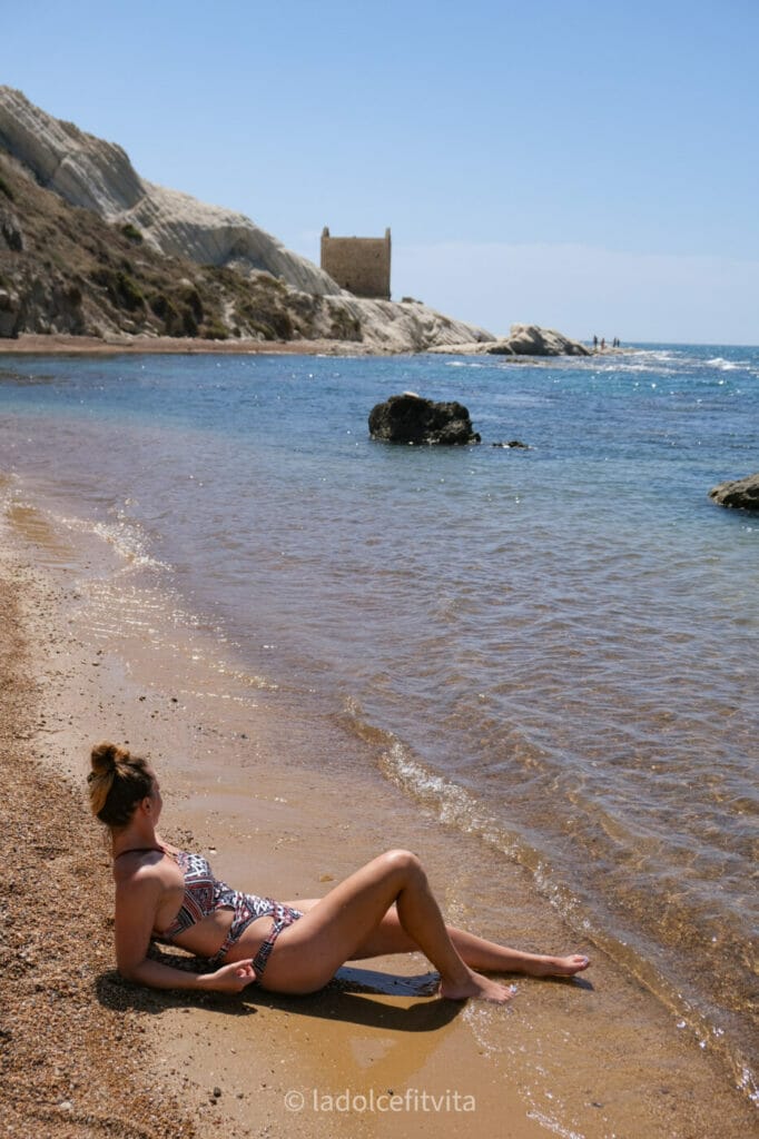 woman lying on a golden sandy beach in Punta Bianca Sicily as she looks at white calcareous rocks in the distance