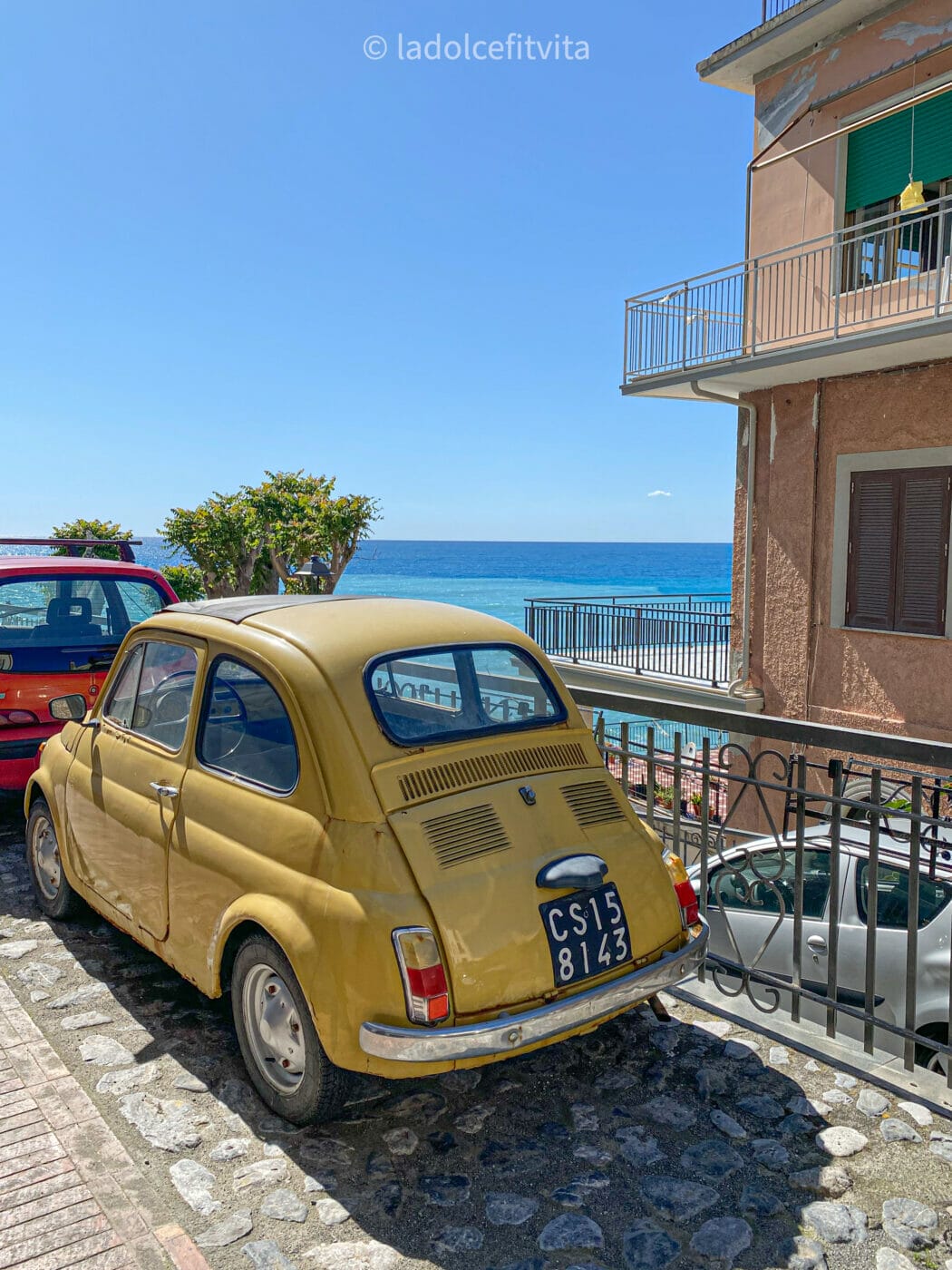 a yellow 500 Fiat car with turquoise sea in the background